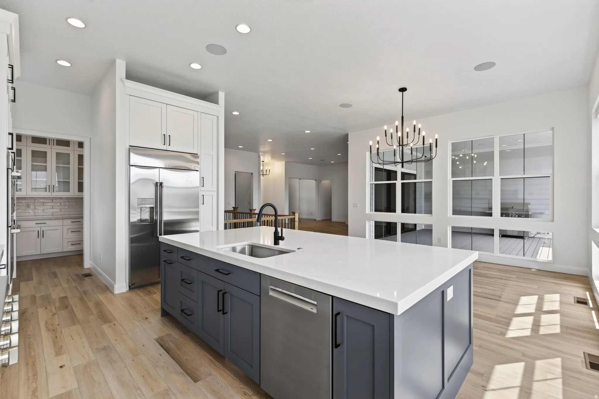 Open-concept kitchen featuring an oversized island with an integrated sink, stainless steel appliances, and wood-finish flooring