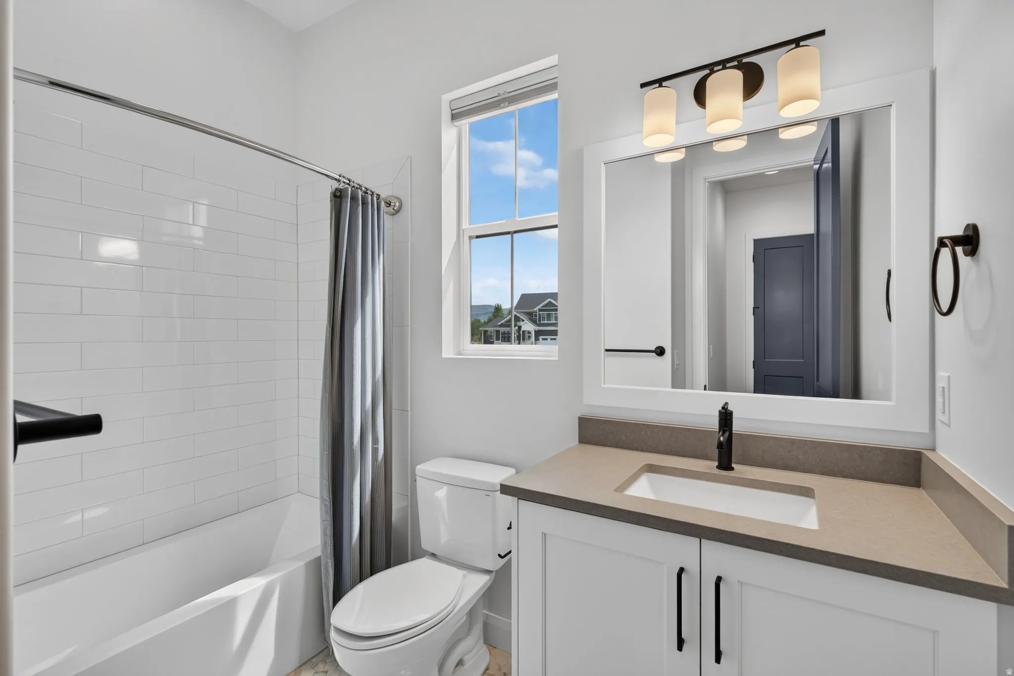 Bathroom featuring a built-in tub with subway tile surround, single vanity with integrated sink and stone-finish countertop, and a framed mirror with a three-light fixture