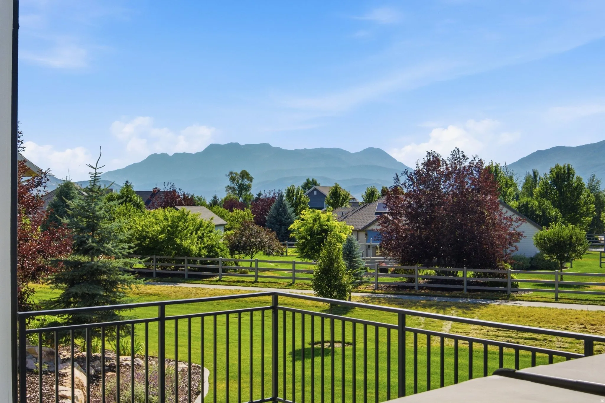 Balcony with black metal railing overlooking a landscaped green space, perimeter fencing, and distant mountain range