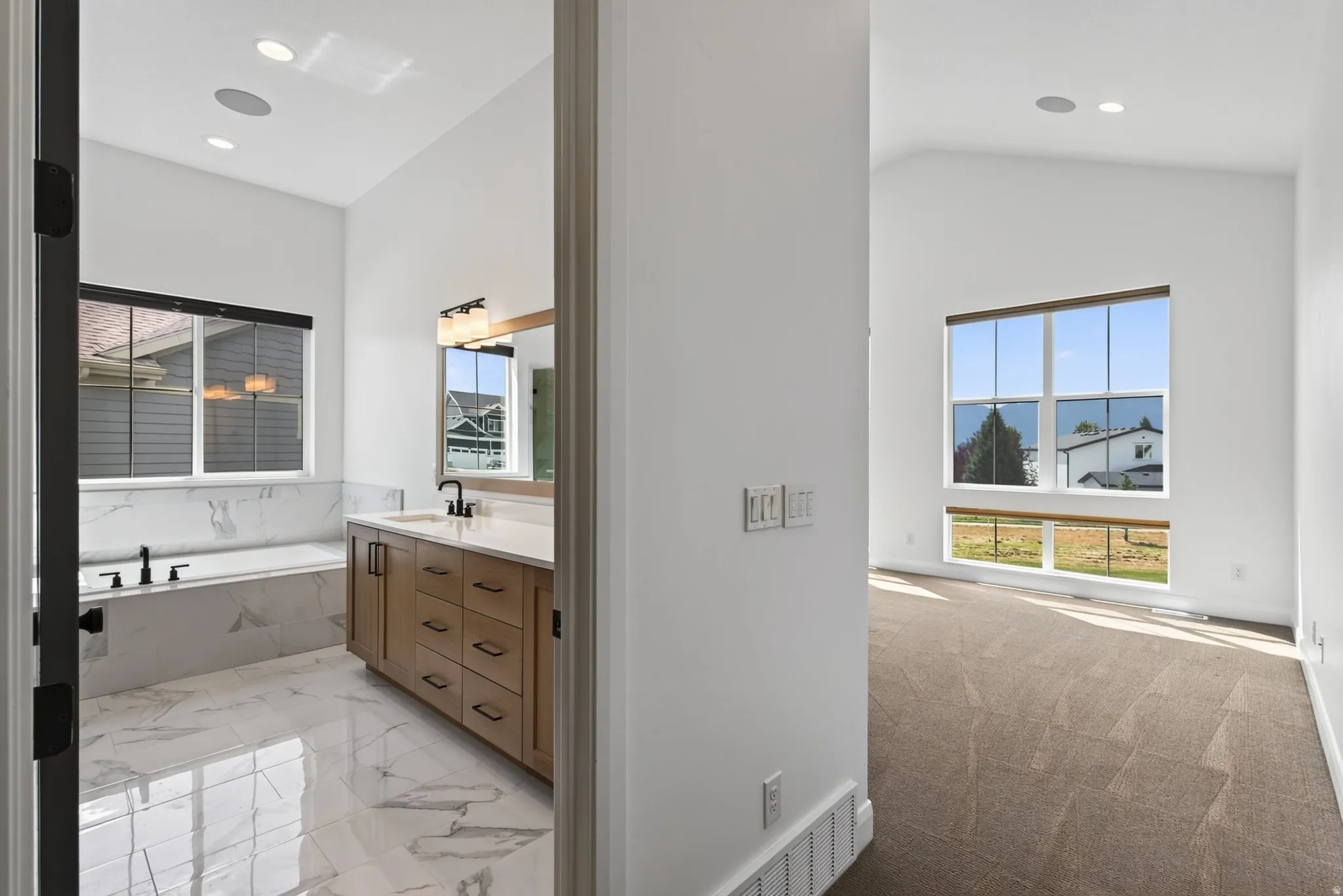 Spacious bathroom featuring a built-in tub with marble-finish tile surround, a wood-finish vanity with a light-toned countertop, and recessed lighting