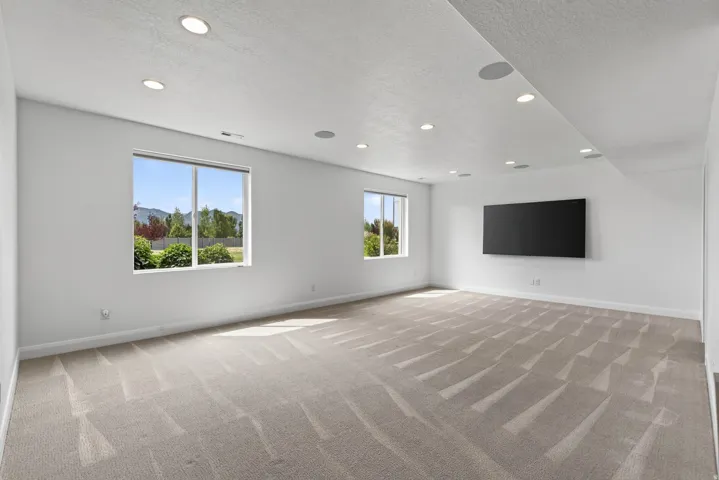 Spacious room featuring light-toned carpeting, recessed ceiling lighting, and multiple windows