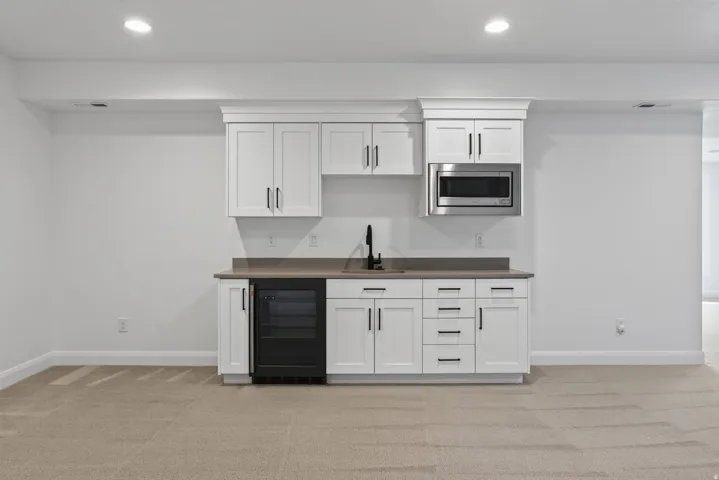 Built-in wet bar featuring white cabinetry, a stone-finish countertop, stainless steel microwave, black beverage refrigerator, and a matte black faucet