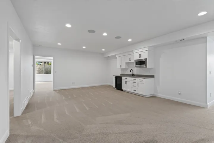 Spacious open-concept room featuring a built-in wet bar with white cabinetry, a black sink, and a stainless steel microwave