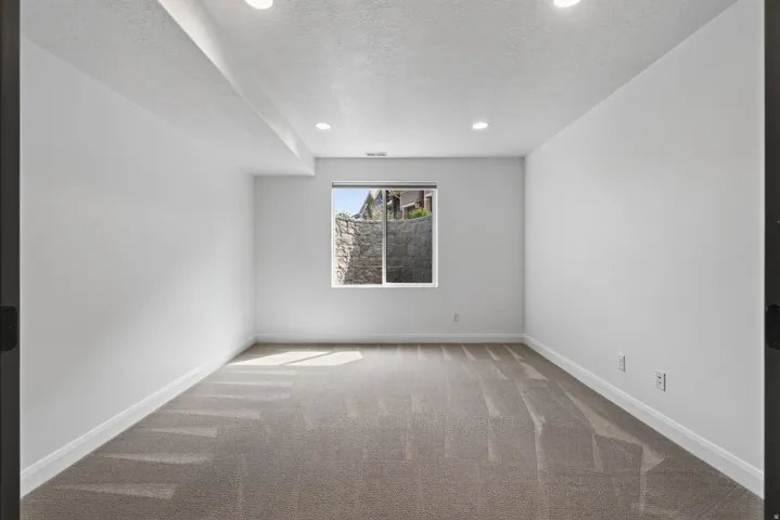 Spacious room featuring neutral carpeting, white walls, recessed lighting, and a window with natural light