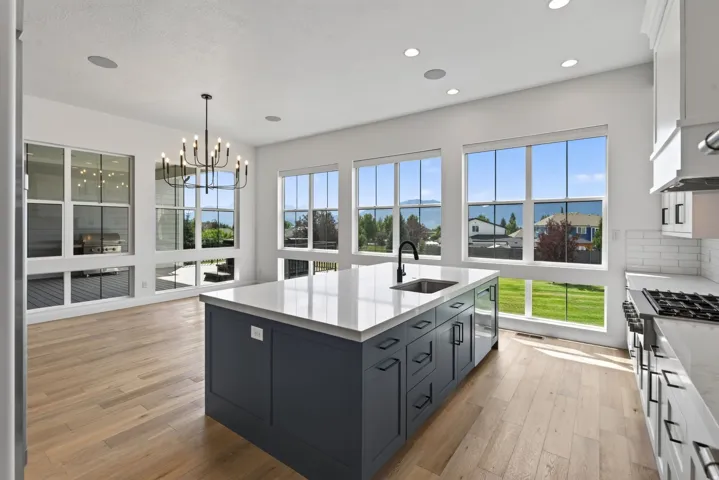 Bright kitchen featuring a central island with an integrated sink, expansive windows, light wood-finish flooring, white subway tile backsplash, and recessed lighting