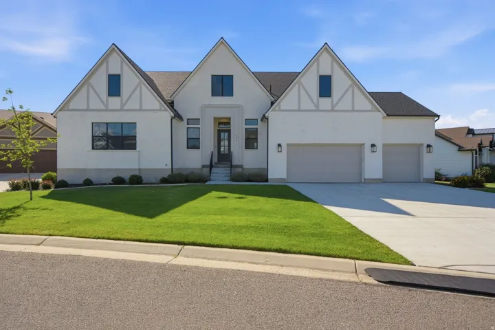 Stately residence featuring a white brick and stucco exterior with dark trim accents, a prominent gabled roofline, a two-car garage, an additional single-car garage, and a concrete driveway