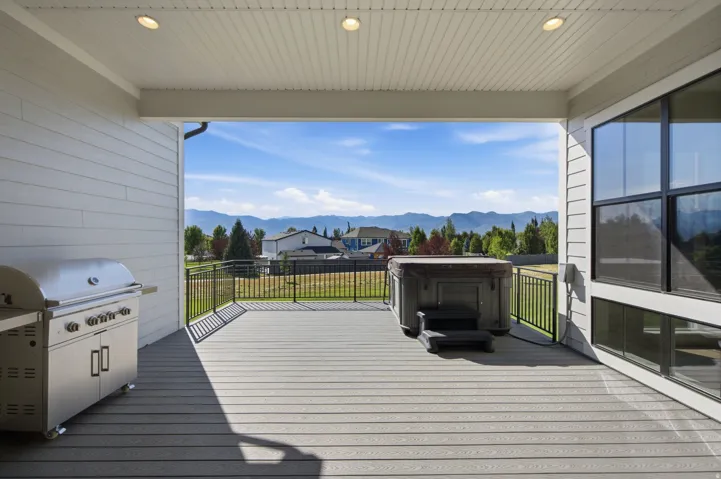 Covered composite deck featuring a hot tub, stainless steel barbecue grill, and black metal railings