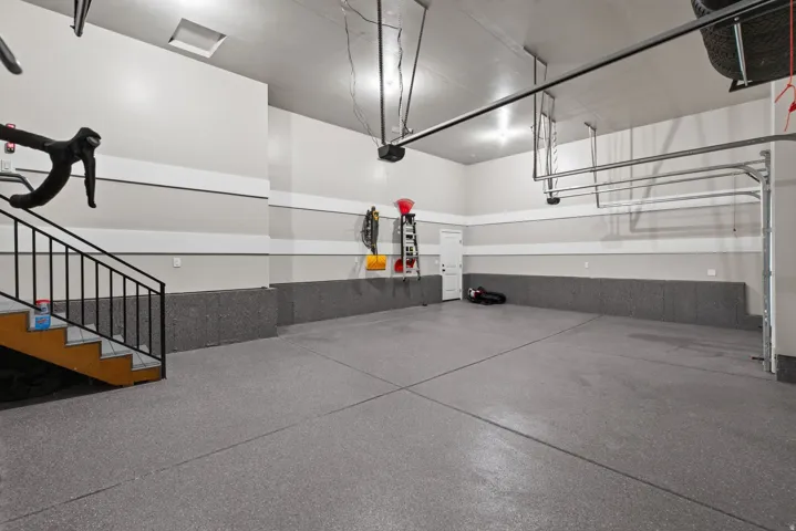 Spacious two-car garage with epoxy flooring, finished walls, and a staircase providing internal access
