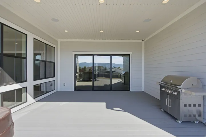 Expansive covered patio featuring light gray decking, recessed lighting, and integrated ceiling speakers