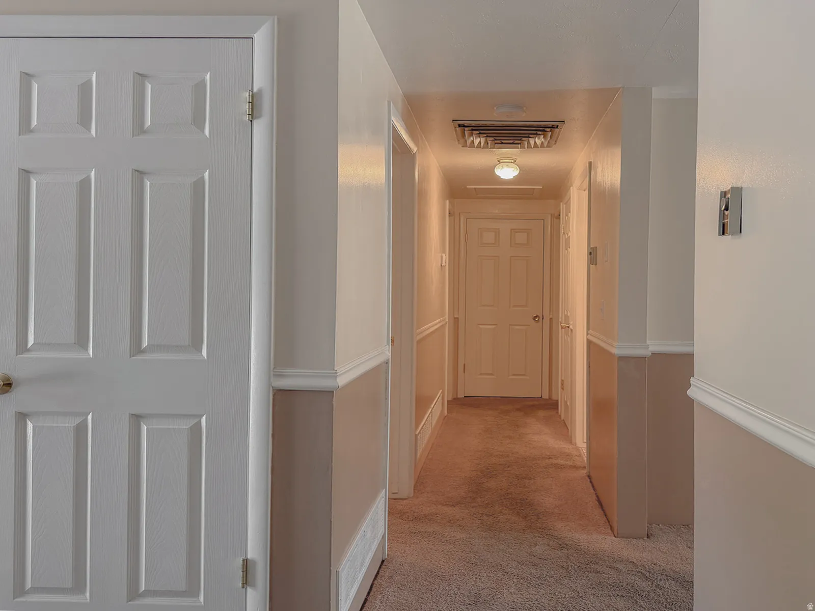 Hallway featuring panel doors, neutral two-tone painted walls, crown molding, and carpet flooring