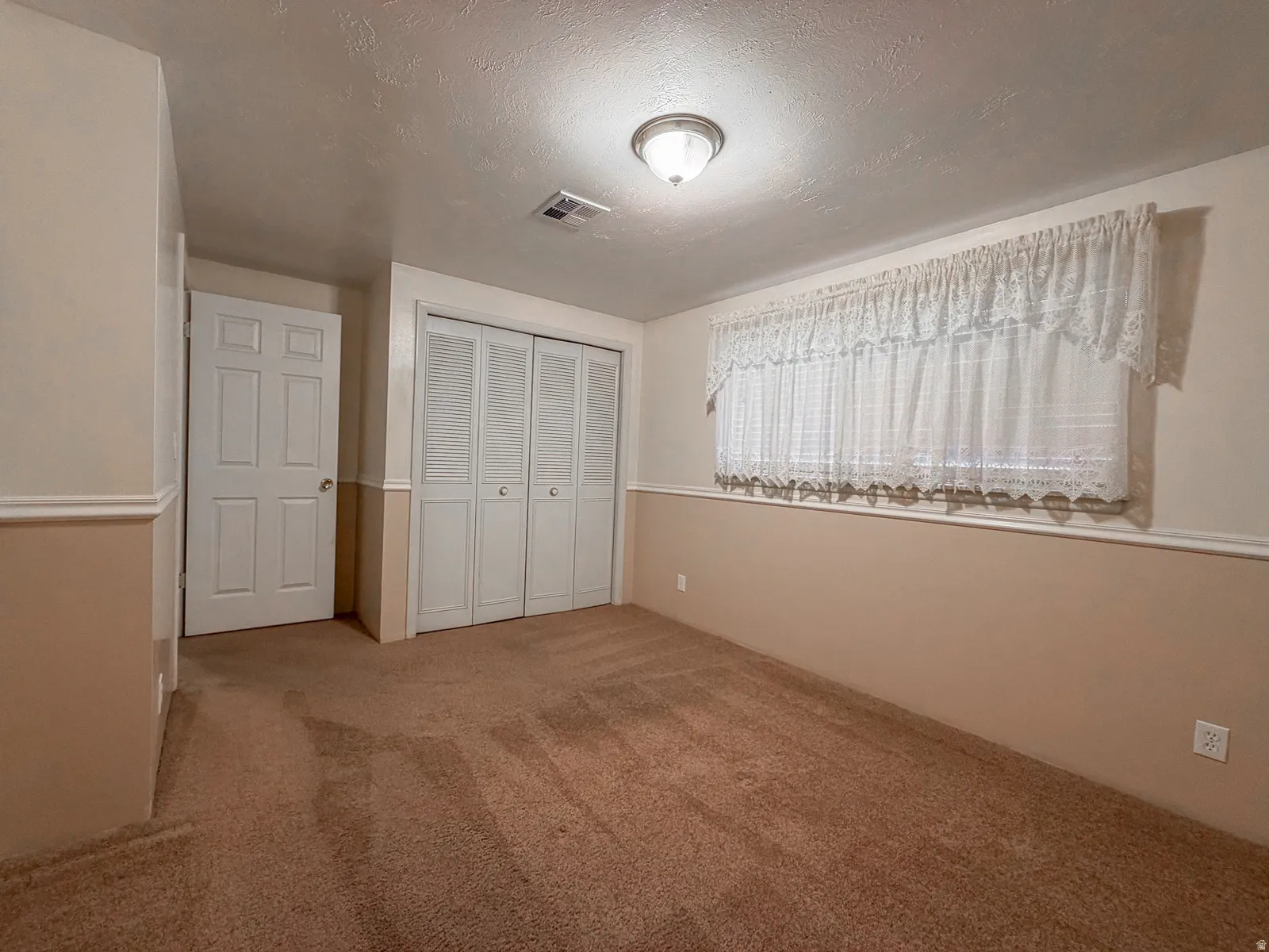Carpeted room with a wall-mounted light fixture, white interior door, and bi-fold closet doors