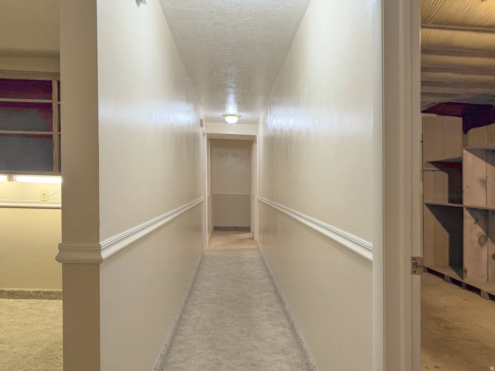 Carpeted hallway featuring chair rail molding, ceiling-mounted lighting, and neutral wall paint