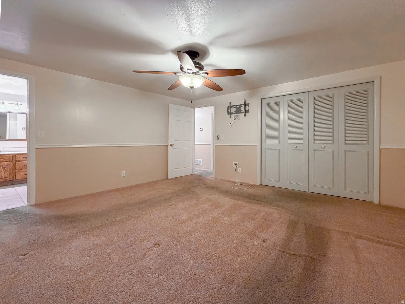 Carpeted room with a ceiling fan light fixture, bi-fold closet doors, and two-tone wall paneling