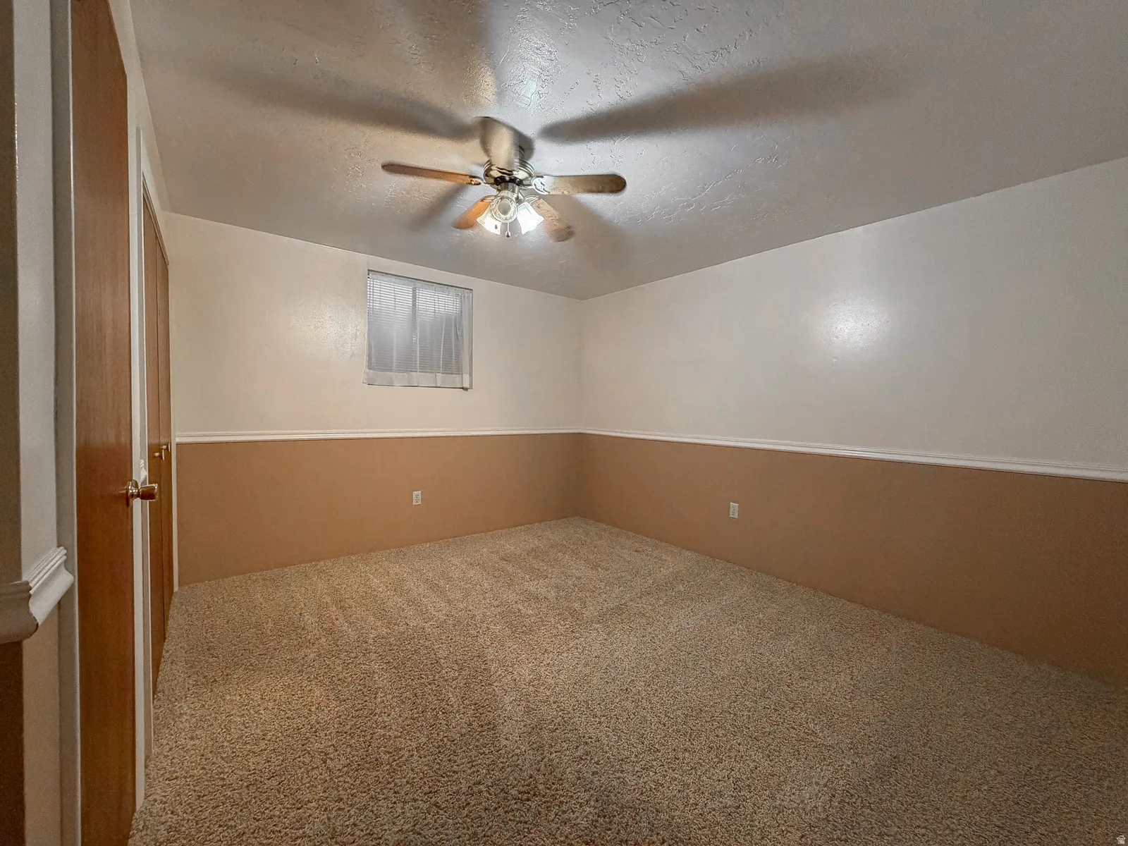 Carpeted room featuring a ceiling fan with integrated lighting, wood-finish doors, a window with horizontal blinds, and a two-tone wall treatment