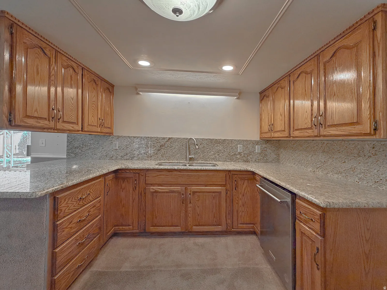 U-shaped kitchen featuring wood cabinetry, light-toned countertops with a matching backsplash, a stainless steel dishwasher, and a double-basin sink