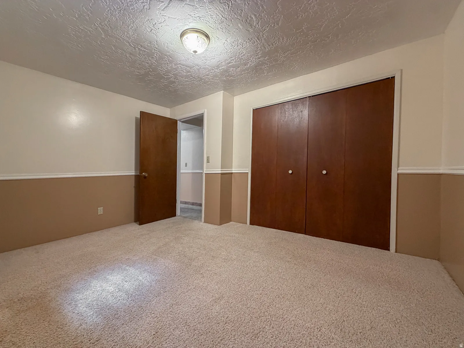Carpeted room featuring a two-tone wall treatment with a chair rail, a wood-panel bi-fold closet, and a semi-flush mount ceiling light fixture