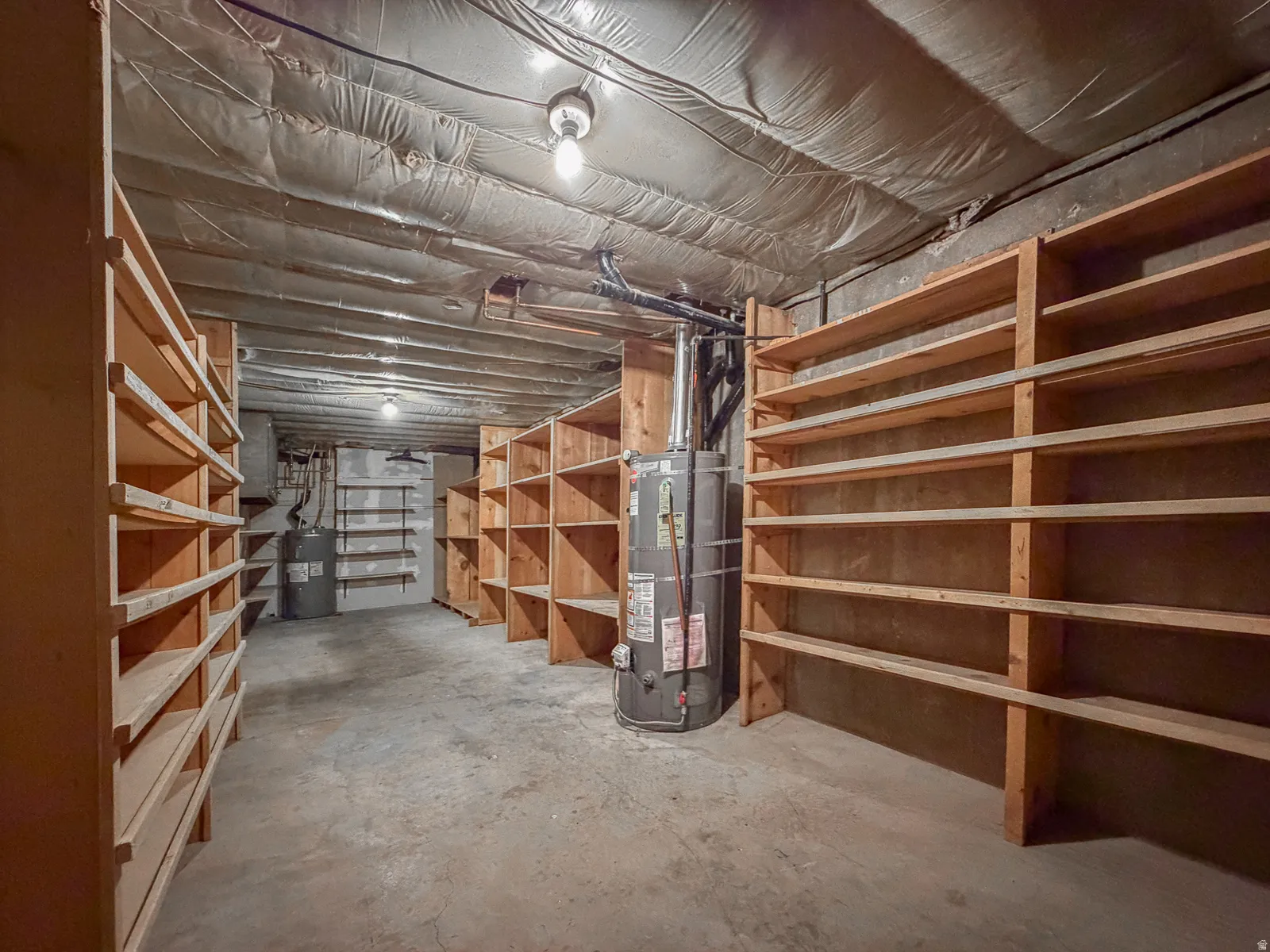 Basement storage area featuring extensive built-in wooden shelving, concrete flooring, and exposed ceiling joists with insulation