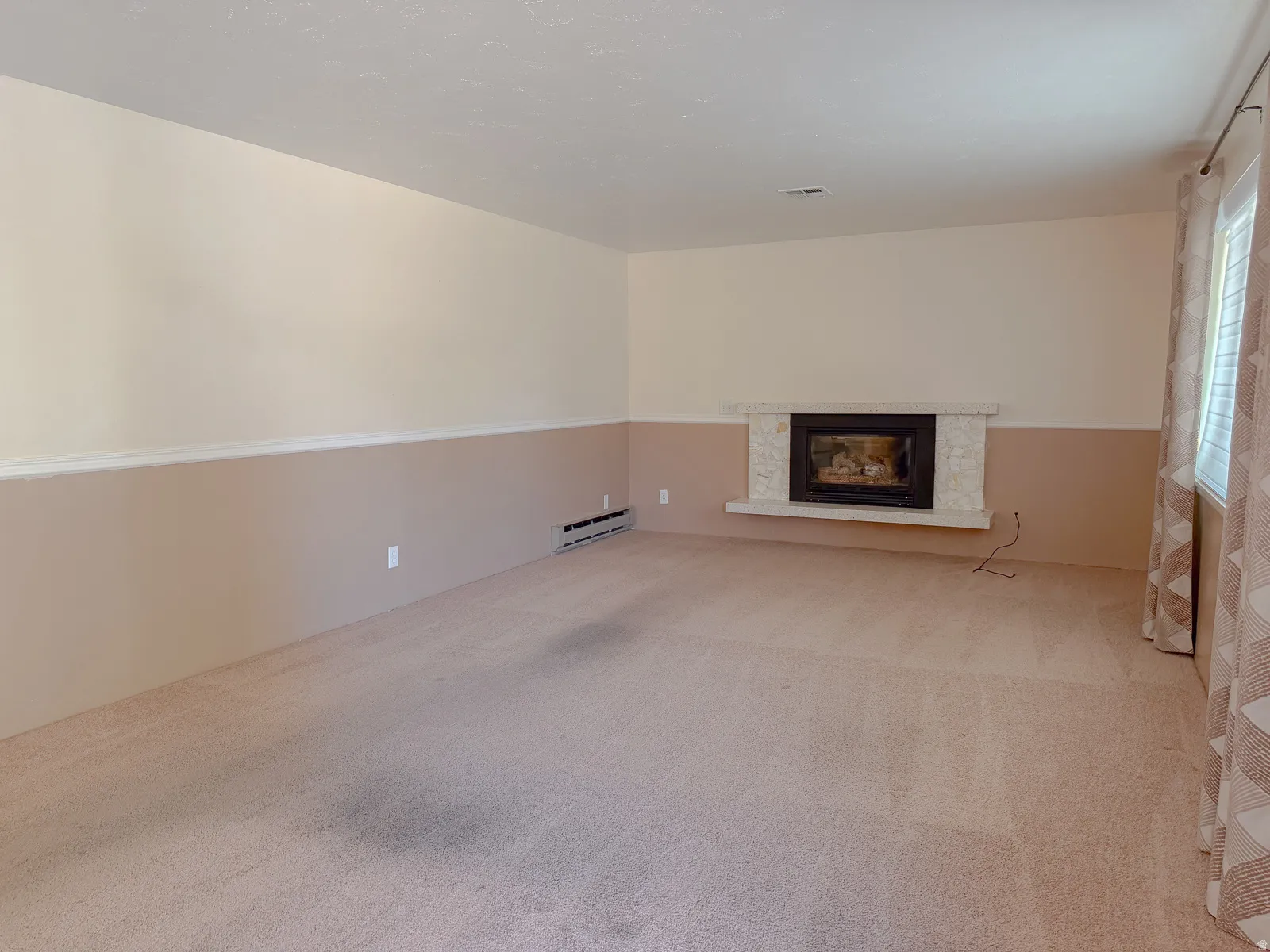 Spacious room featuring a stone-clad fireplace with a black insert, light-colored carpeting, and a window with blinds