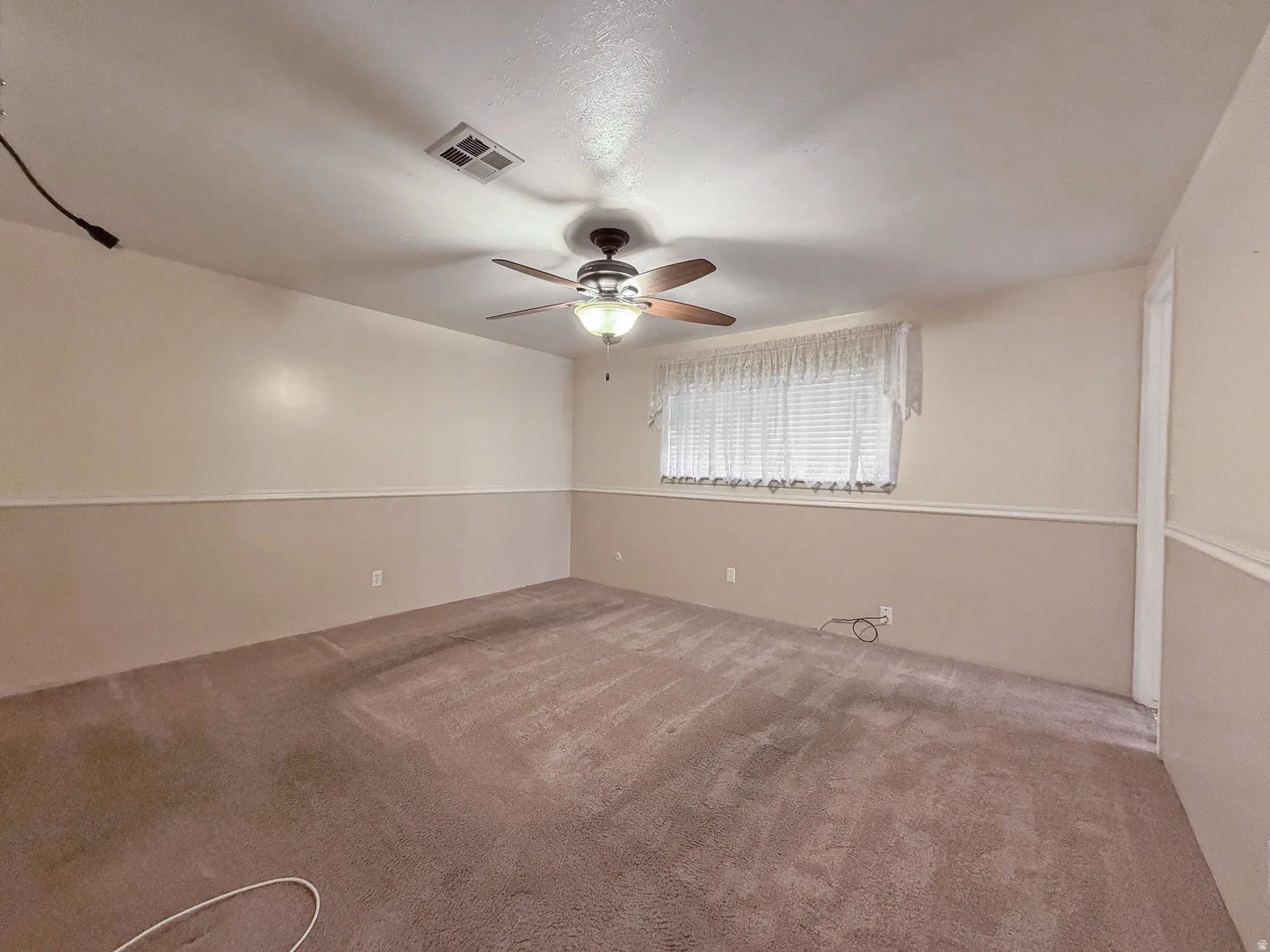 Spacious room featuring neutral-toned carpeting, a ceiling fan with integrated lighting, and a window with blinds