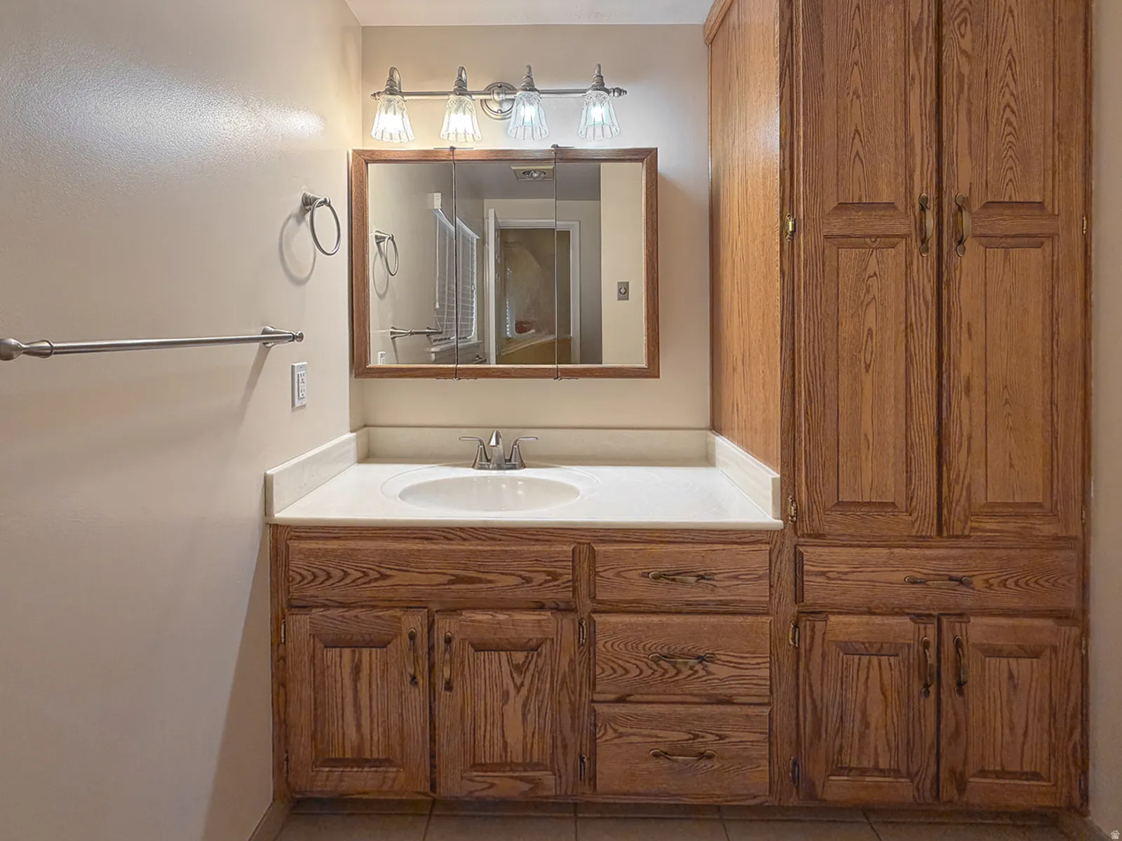 Bathroom vanity with a white countertop and integrated sink, complemented by wood-finish cabinetry