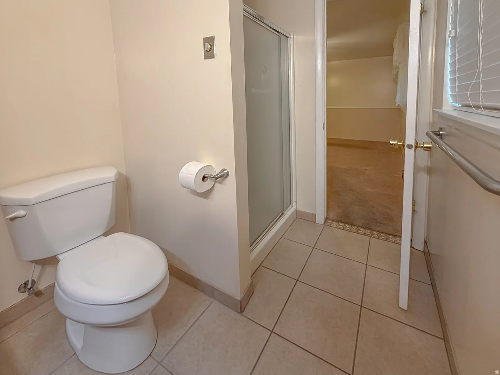 Bathroom featuring a white toilet, tile flooring, glass-enclosed shower, window with blinds, and a grab bar