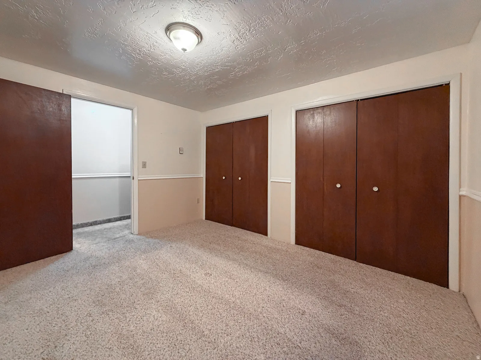 Carpeted room featuring multiple dark wood-finish bi-fold closet doors, two-tone painted walls with chair rail molding, and an overhead flush-mount light fixture