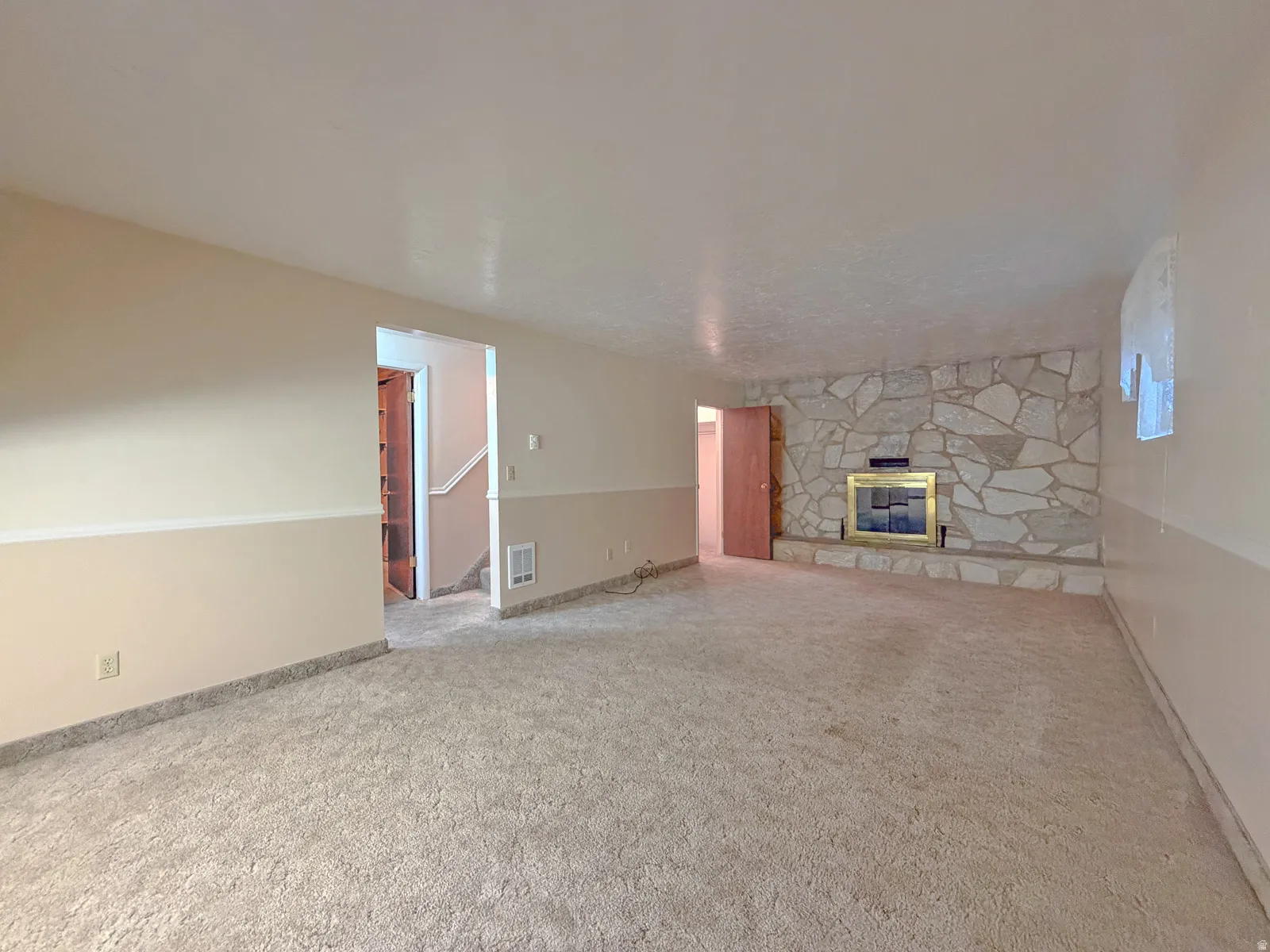 Spacious room featuring a stone-clad fireplace with a brass-toned insert, neutral carpet flooring, and a two-tone wall treatment