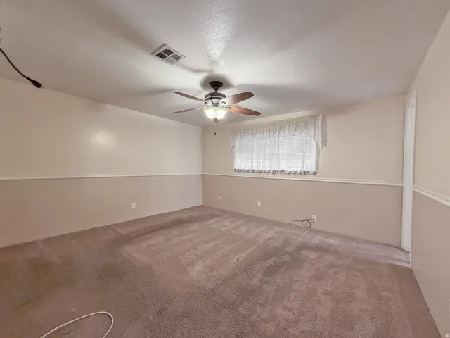 Spacious room featuring neutral-toned carpeting, a ceiling fan with integrated lighting, and a window with blinds