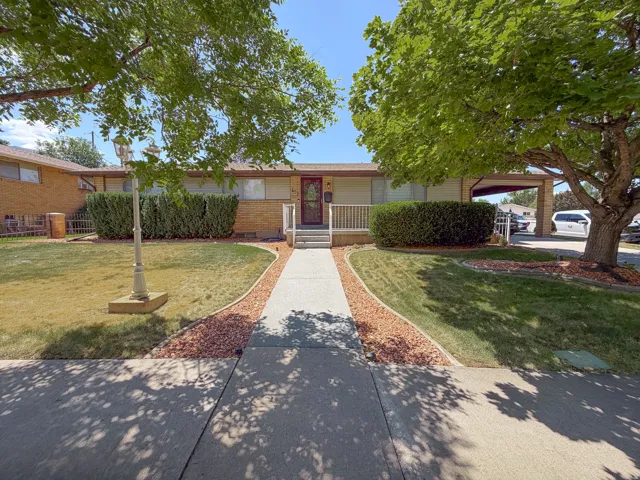 Brick exterior home featuring a covered front porch, carport, and mature trees
