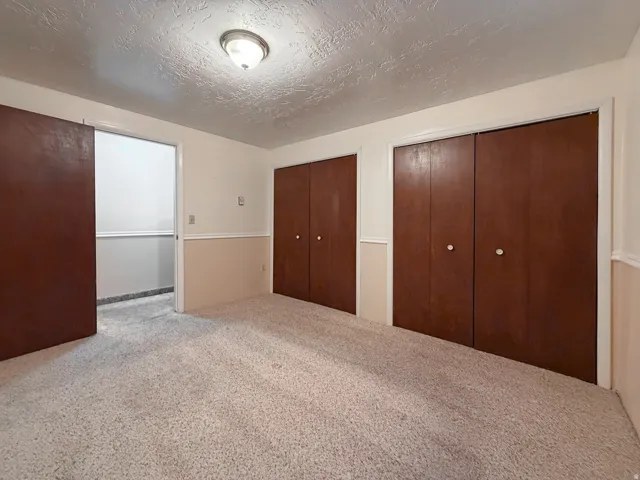 Carpeted room featuring multiple dark wood-finish bi-fold closet doors, two-tone painted walls with chair rail molding, and an overhead flush-mount light fixture