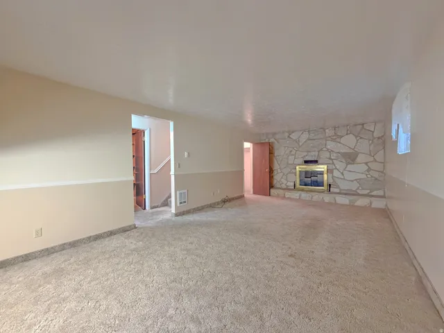 Spacious room featuring a stone-clad fireplace with a brass-toned insert, neutral carpet flooring, and a two-tone wall treatment