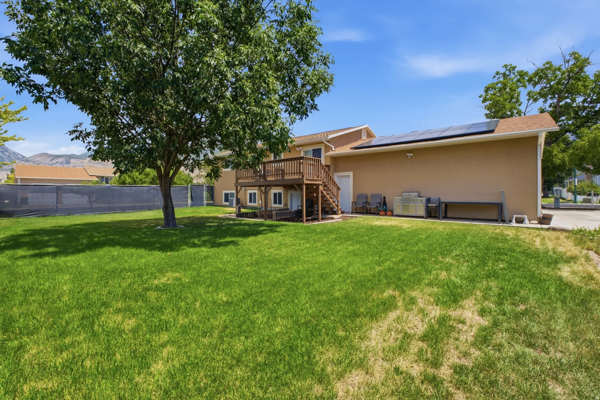 Spacious backyard featuring a multi-level wood deck, ground-level patio, mature shade tree, and solar panels