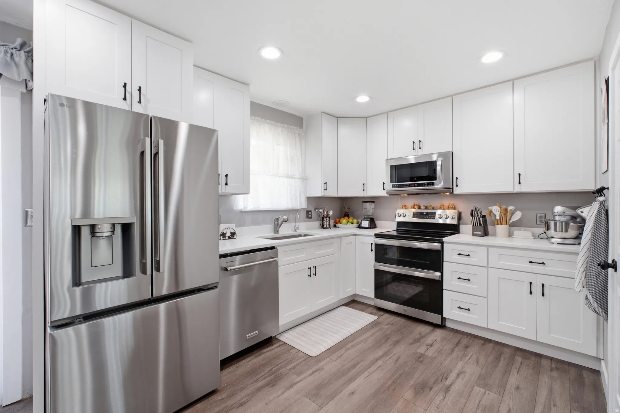 Modern kitchen featuring white shaker cabinetry, stainless steel appliances, light countertops, wood-finish flooring, and recessed lighting