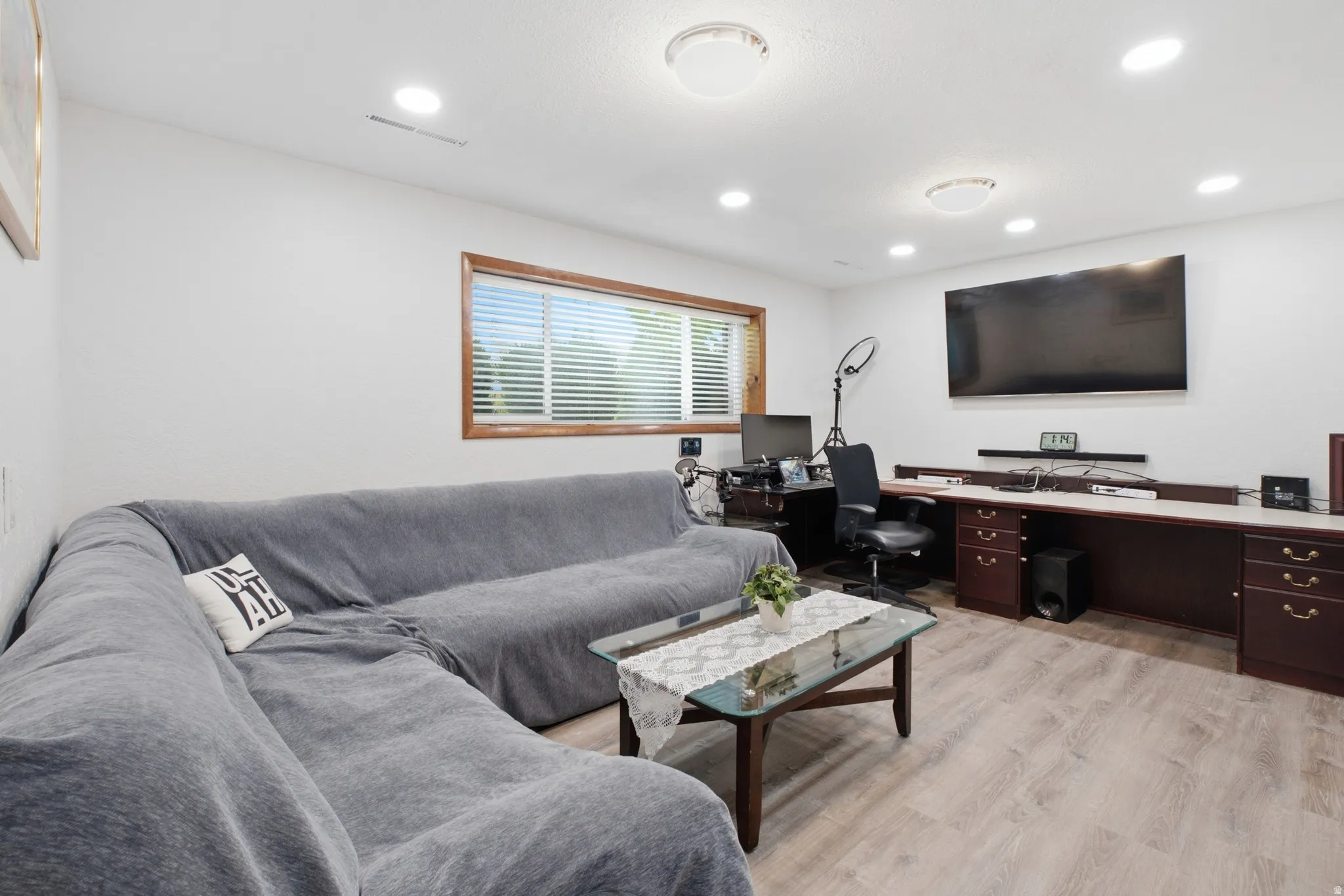 Spacious room featuring light wood-finish flooring, recessed lighting, and a large built-in desk unit with dark wood cabinetry