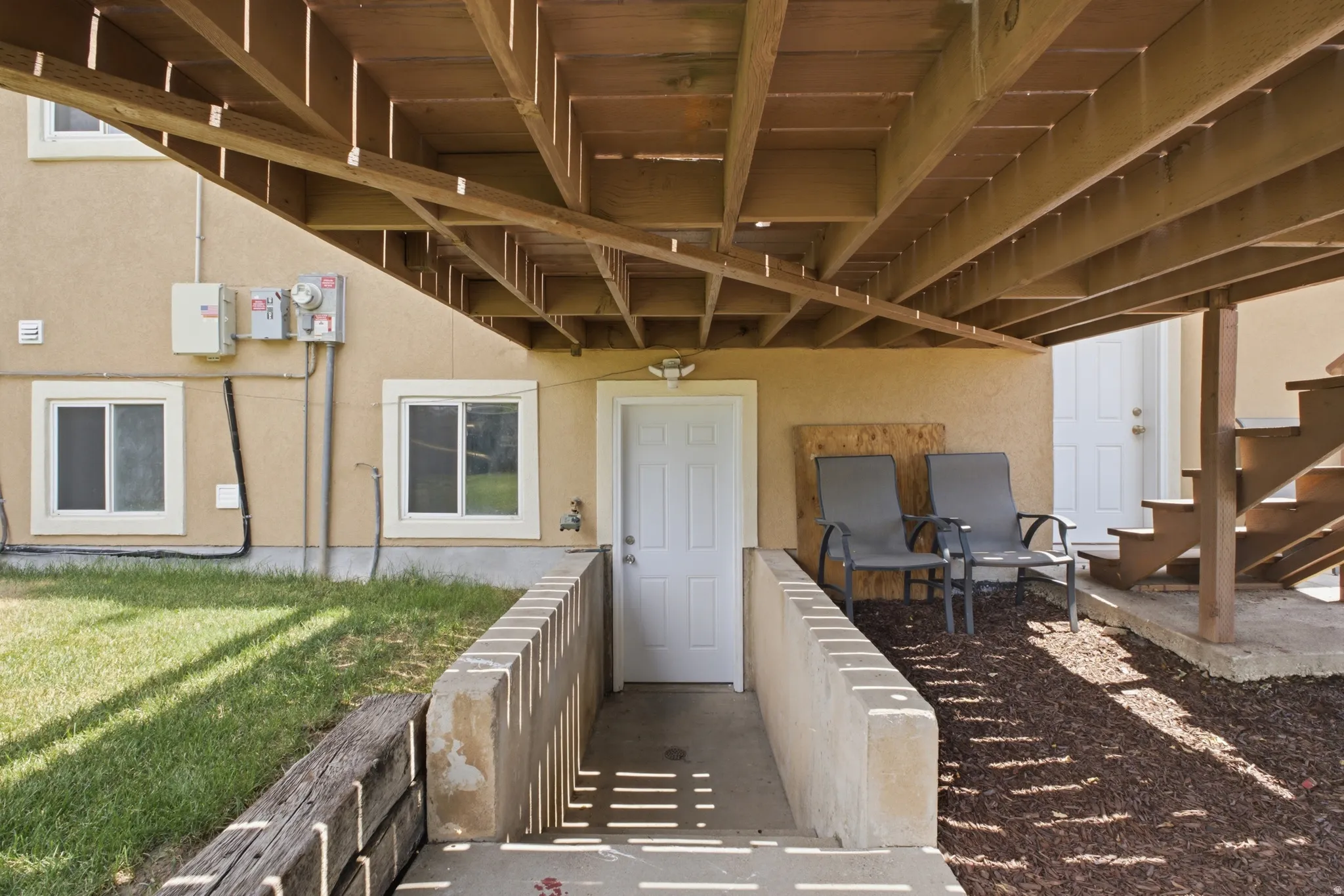 Covered concrete patio area with a white entry door, stucco exterior, and wood deck framing overhead