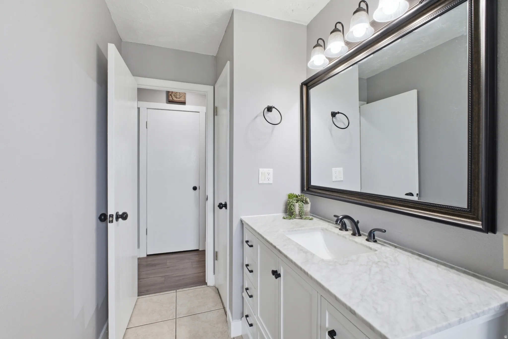 Bathroom vanity featuring a single undermount sink, dark bronze faucet, and a large framed mirror with overhead lighting