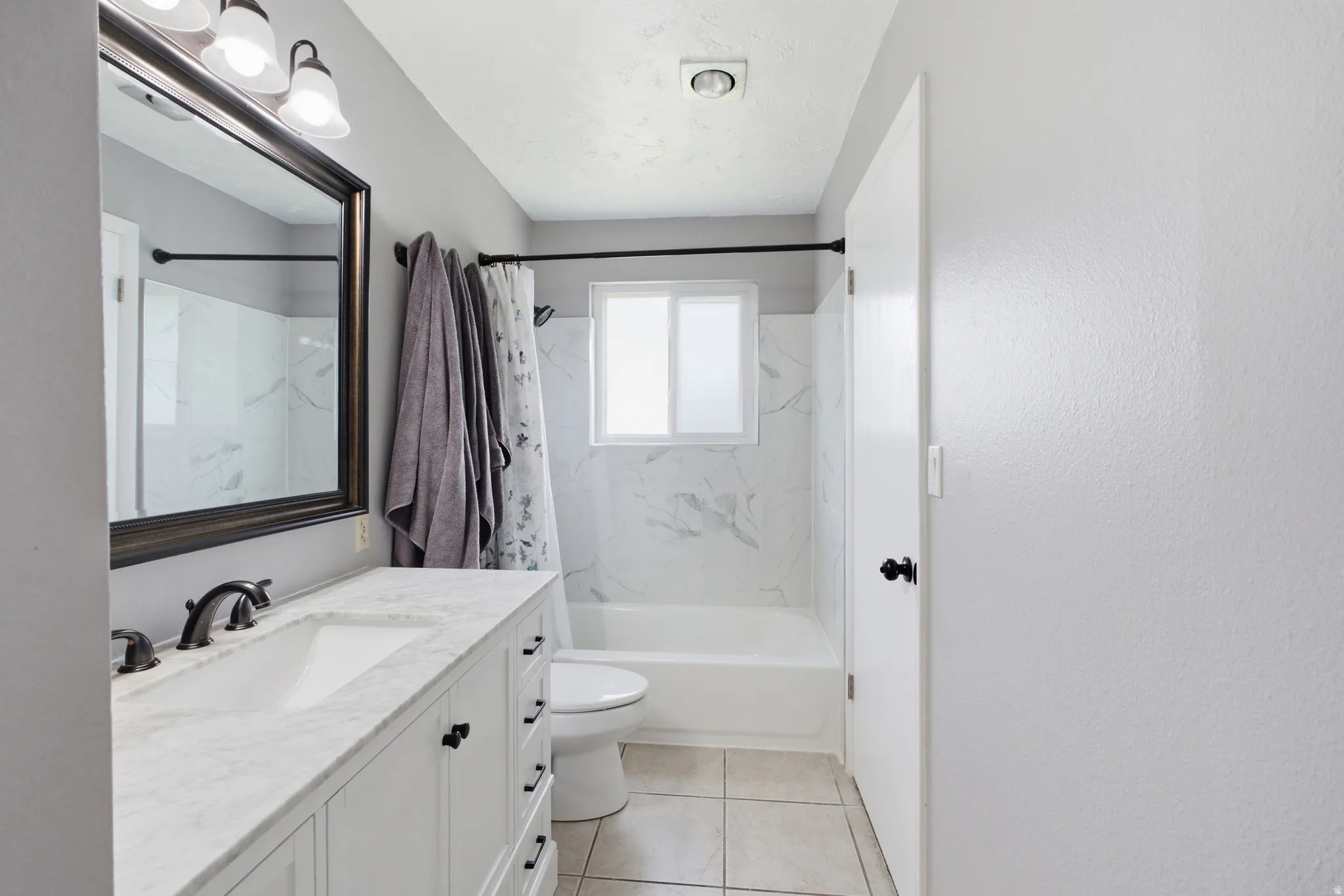 Bathroom featuring a single vanity with a rectangular undermount sink, a stone-finish countertop, and a dark-framed mirror