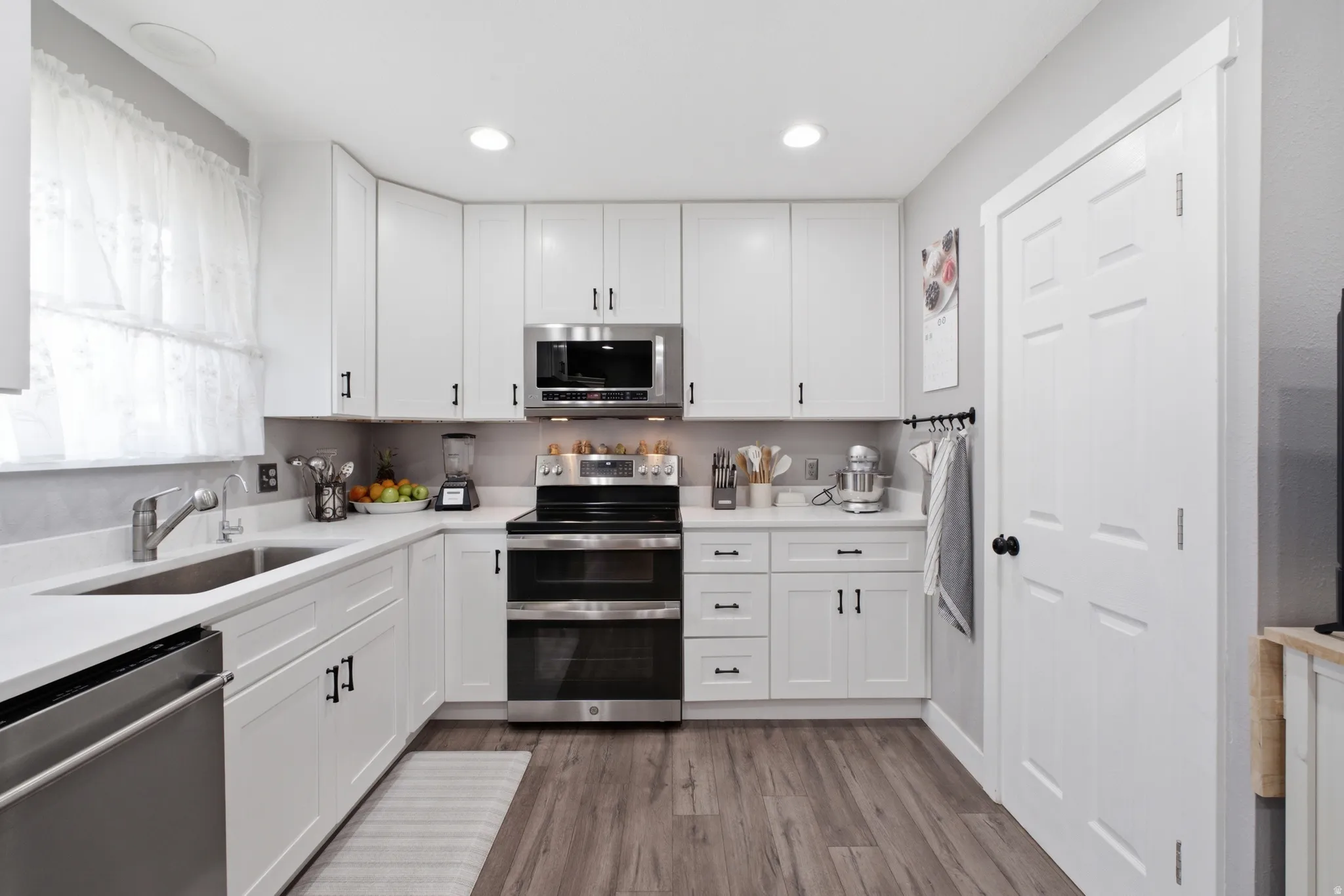 Modern kitchen featuring white cabinetry, stainless steel appliances, a double basin sink, light-toned countertops, and wood-finish flooring