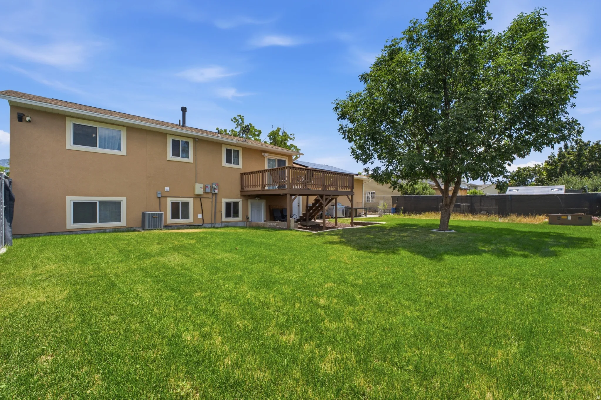 Expansive green lawn with a mature shade tree and a multi-level wooden deck