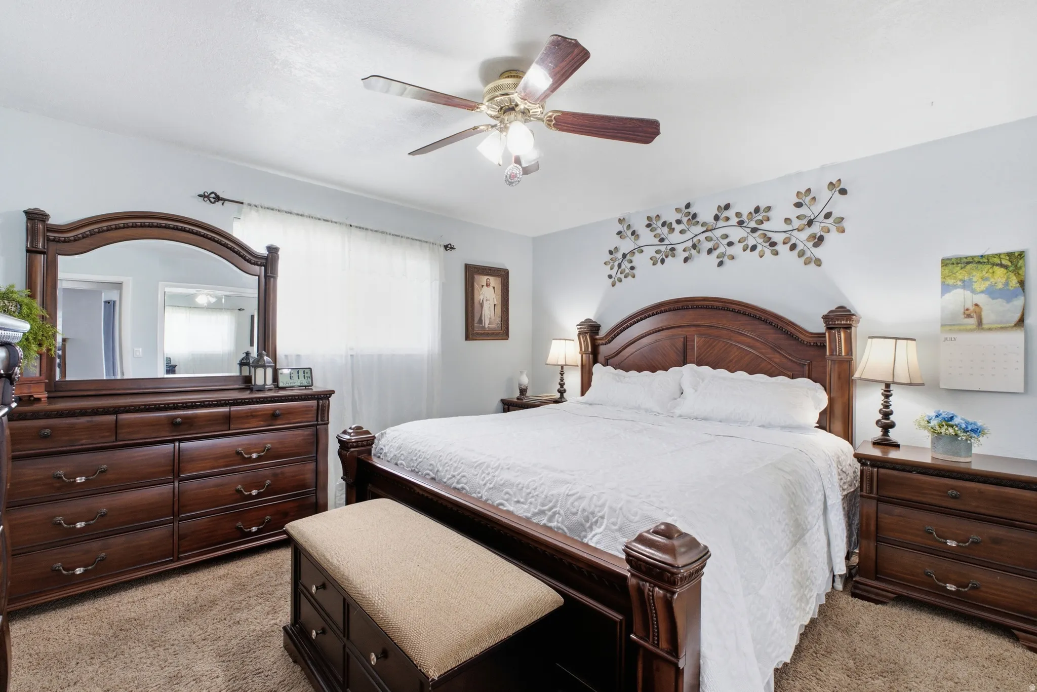 Ceiling fan with light kit, soft wall color, window with privacy sheers, textured carpeting, and decorative wall art