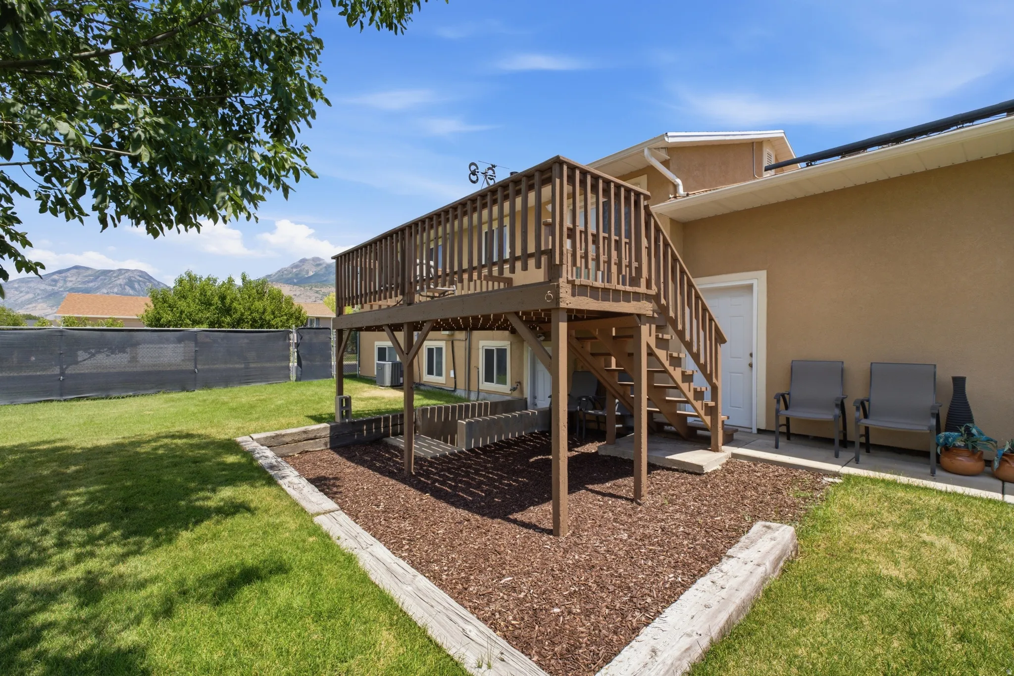 Expansive backyard featuring a wood deck with stairs, a manicured lawn, and a natural mountain backdrop