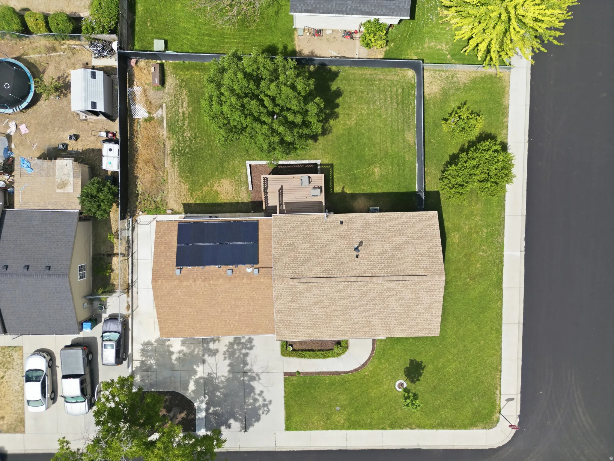 Property featuring a light brown shingle roof, solar panel installation, a concrete driveway, a front lawn with a walkway, and a fenced backyard with grass and mature trees