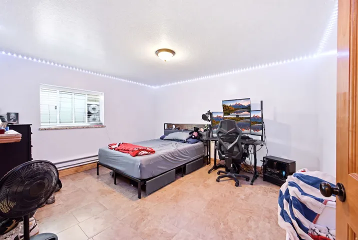 Main home - Bedroom featuring tile flooring, white walls, and a window with blinds