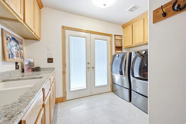 Main home - Laundry area with a utility sink, light wood-finish cabinetry, granite-finish countertops, and double glass-paned doors