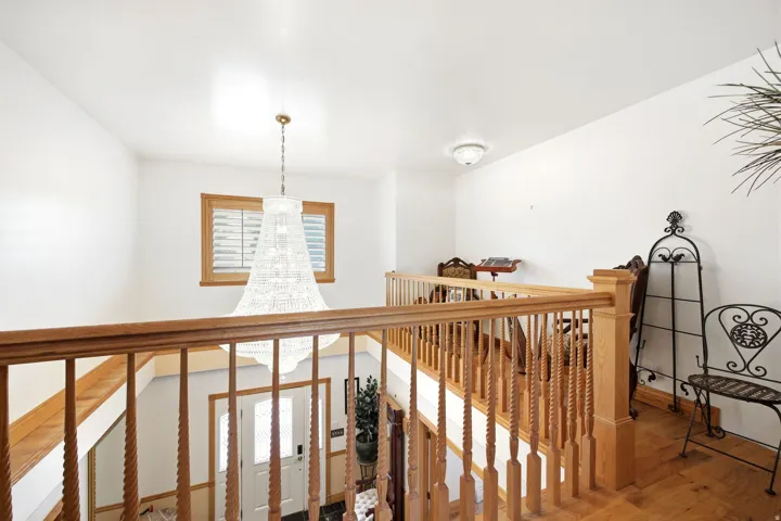 Main home - Vaulted ceiling foyer featuring a chandelier, wood-finish flooring, and a wooden staircase with balusters