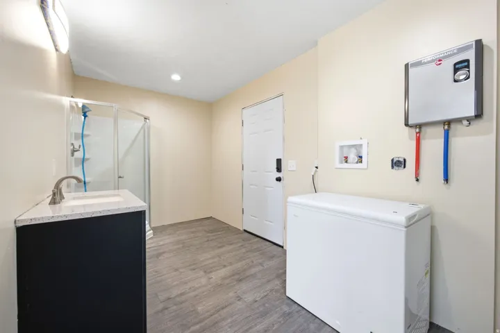 ADU - Utility room featuring wood-finish flooring, a glass-enclosed shower, and a vanity with a white countertop and undermount sink