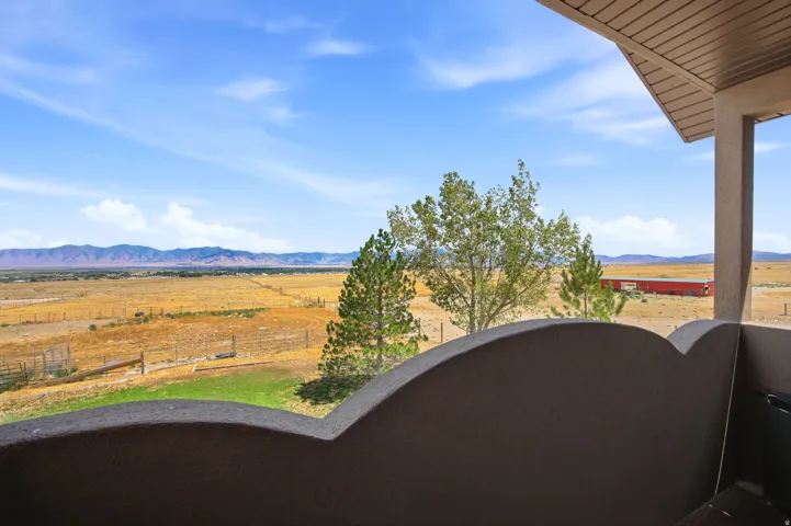 Main home - Master bedroom with outdoor balcony with a textured stucco railing and an overhead soffit, offering a panoramic landscape of distant mountains, a wide field, and scattered trees
