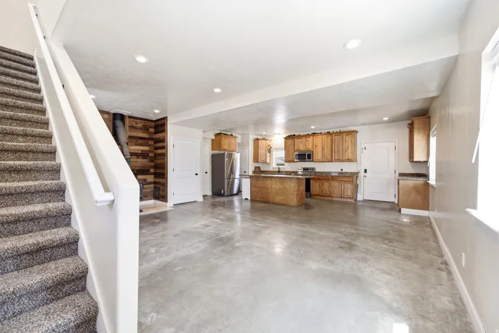 ADU - Open-concept living area featuring polished concrete flooring, a wood-paneled accent wall with a stove, and a kitchen with wood cabinetry, stone-look countertops, and stainless steel appliances