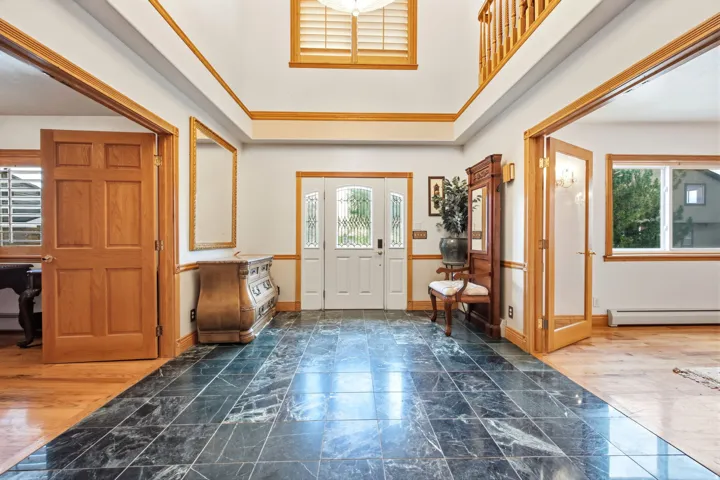 Main home - Grand foyer featuring dark stone tile flooring, a two-story ceiling, and natural wood trim throughout