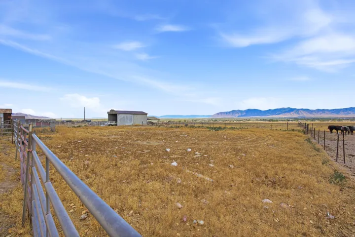 Expansive open land featuring a metal storage building, perimeter fencing, and distant mountain ranges